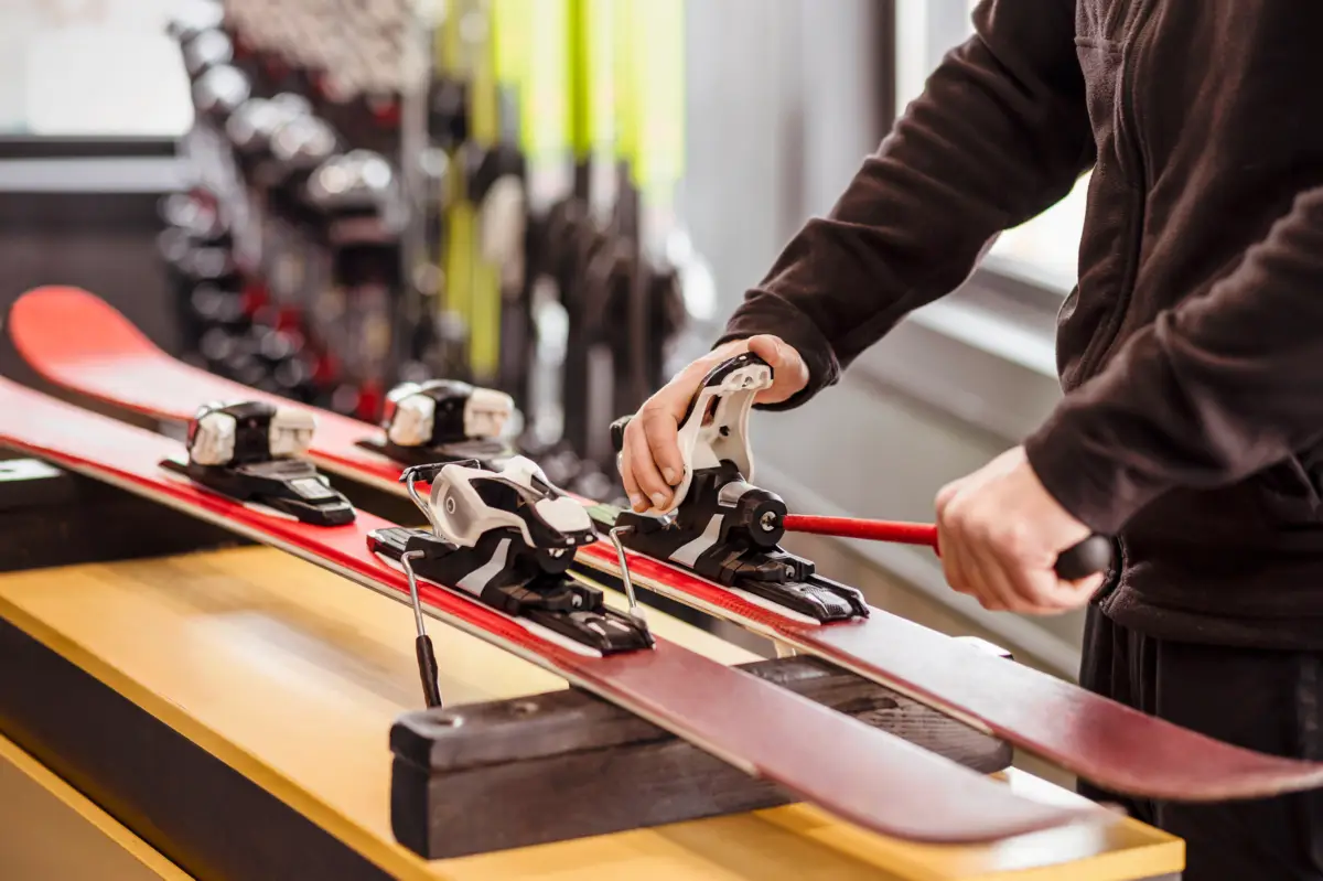 Un technicien ajuste des fixations sur des skis rouges posés sur un établi, à l'intérieur d'un magasin de ski.